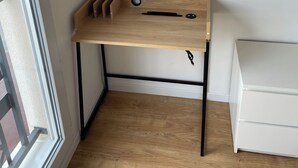 A corner room with a wooden desk, a white drawer unit, and a window. - Appartement Cosy : Paris/cdg/ Parking Prive (Le Blanc-Mesnil)