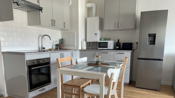 A modern kitchen with white cabinets, a built-in oven, a microwave, and a refrigerator. - Appartement Cosy : Paris/cdg/ Parking Prive (Le Blanc-Mesnil)