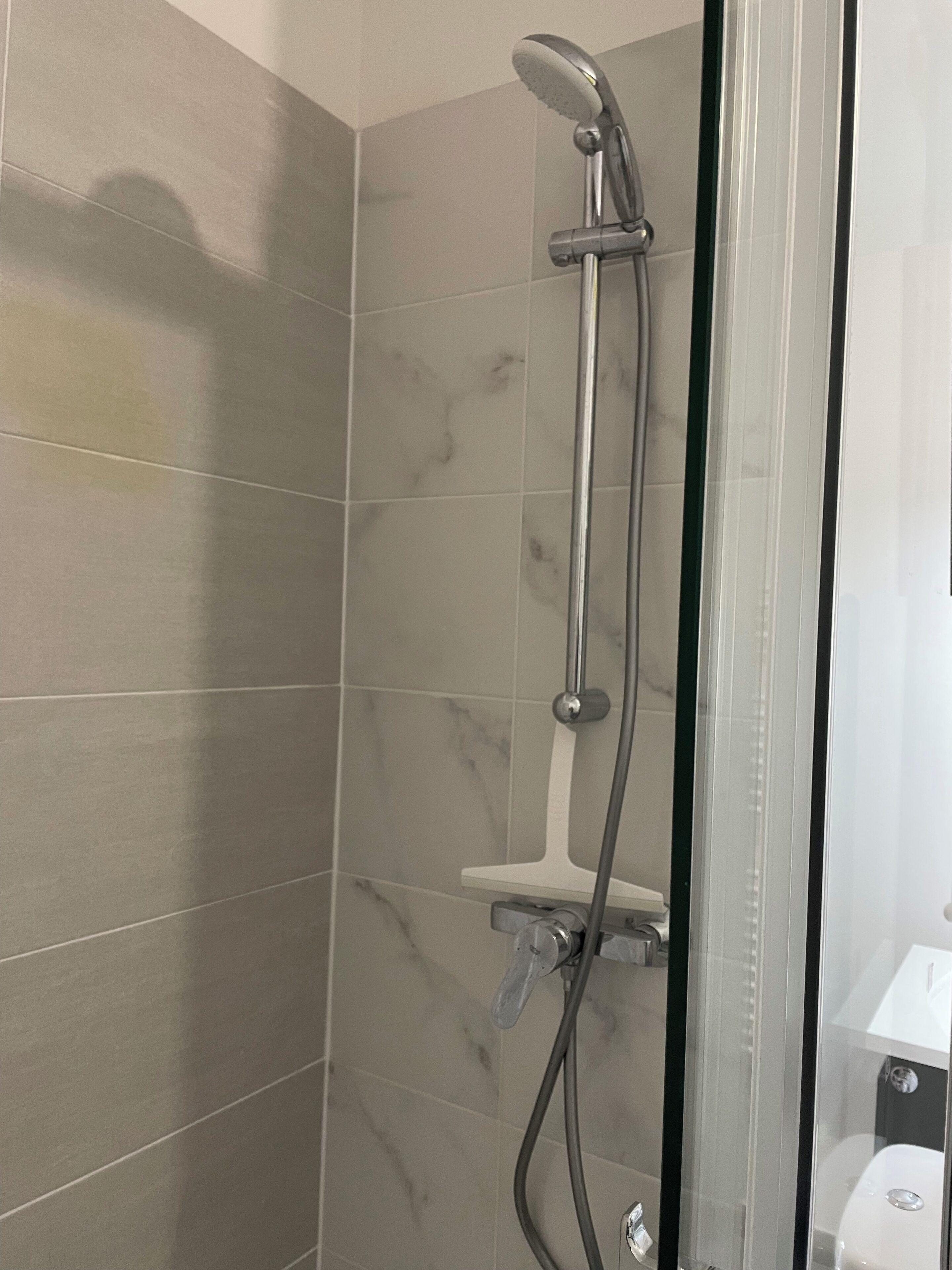 A shower with a handheld showerhead and a wall-mounted faucet.