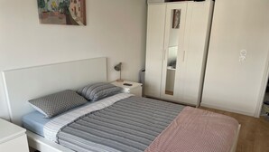 A neatly arranged bedroom with a bed, bedside tables, a wardrobe, and a painting on the wall. - Appartement Cosy : Paris/cdg/ Parking Prive (Le Blanc-Mesnil)