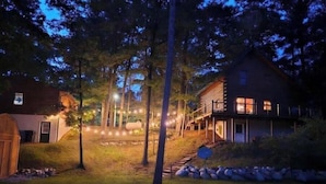 A house with a wooden exterior, a deck, and a stone pathway leading to the entrance. - Premium Lakefront Log Cabin ~ORV (West Branch)