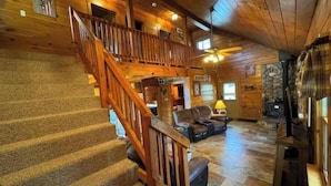 A log cabin interior with a wooden staircase, a stone fireplace, and a cozy seating area. - Premium Lakefront Log Cabin ~ORV (West Branch)