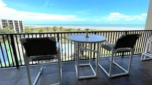 Un balcón con dos sillas y una mesa, con vista a una playa y una piscina.