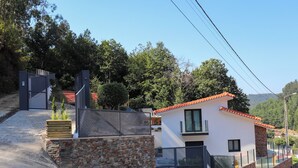 A modern house with a stone wall, a car parked in the driveway, and a clear view of the surrounding trees and hills. - Maison d une Chambre Pour 4 Personnes (Arouca)