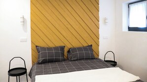 A bedroom with a bed, two bedside tables, a window, and a wall with a wooden panel design. - Maison d une Chambre Pour 4 Personnes (Arouca)