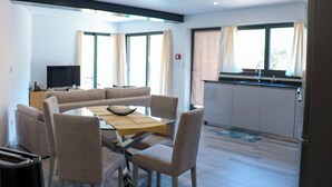 A modern living room with a sofa, a dining table with chairs, a TV, and a kitchen area with a sink and cabinets. - Maison d une Chambre Pour 4 Personnes (Arouca)
