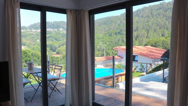 A room with large sliding glass doors leading to an outdoor deck with a pool and a view of a forested hillside. - Maison d une Chambre Pour 4 Personnes (Arouca)