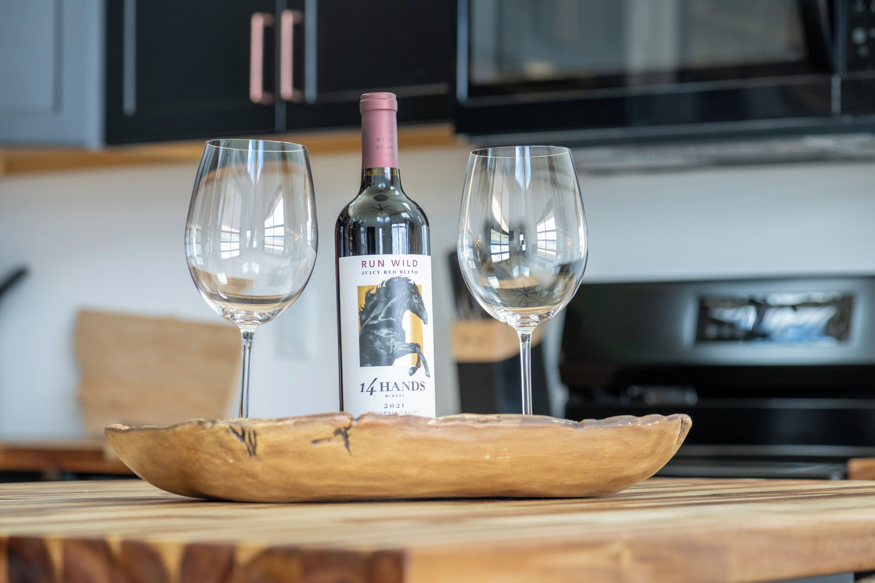 A bottle of Run Wild Juicy Red Blend wine on a wooden tray with two empty wine glasses.
