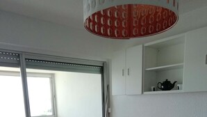 A modern living room with a red sofa, a purple armchair, a glass coffee table, and a sliding glass door leading to a balcony. - Studio VUE MER (Agde)