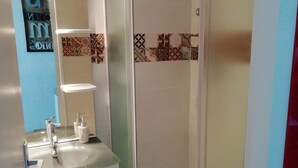 A bathroom with a glass shower enclosure, a sink with a mirror, and a toilet. - Studio VUE MER (Agde)