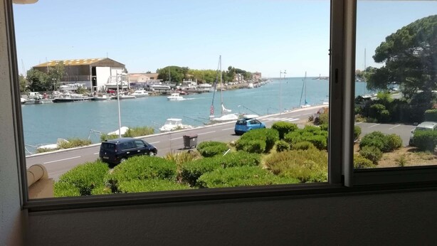 A room with a view of a marina, a table with two candles, and a chair. - Studio VUE MER (Agde)