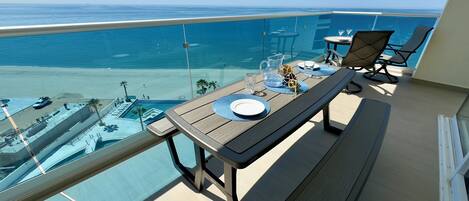 Varanda com mesa posta para dois, com vista para uma piscina e praia.
