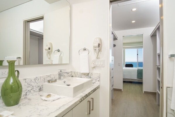 Un baño moderno con encimera de mármol, un florero verde y secadores de pelo montados en la pared.