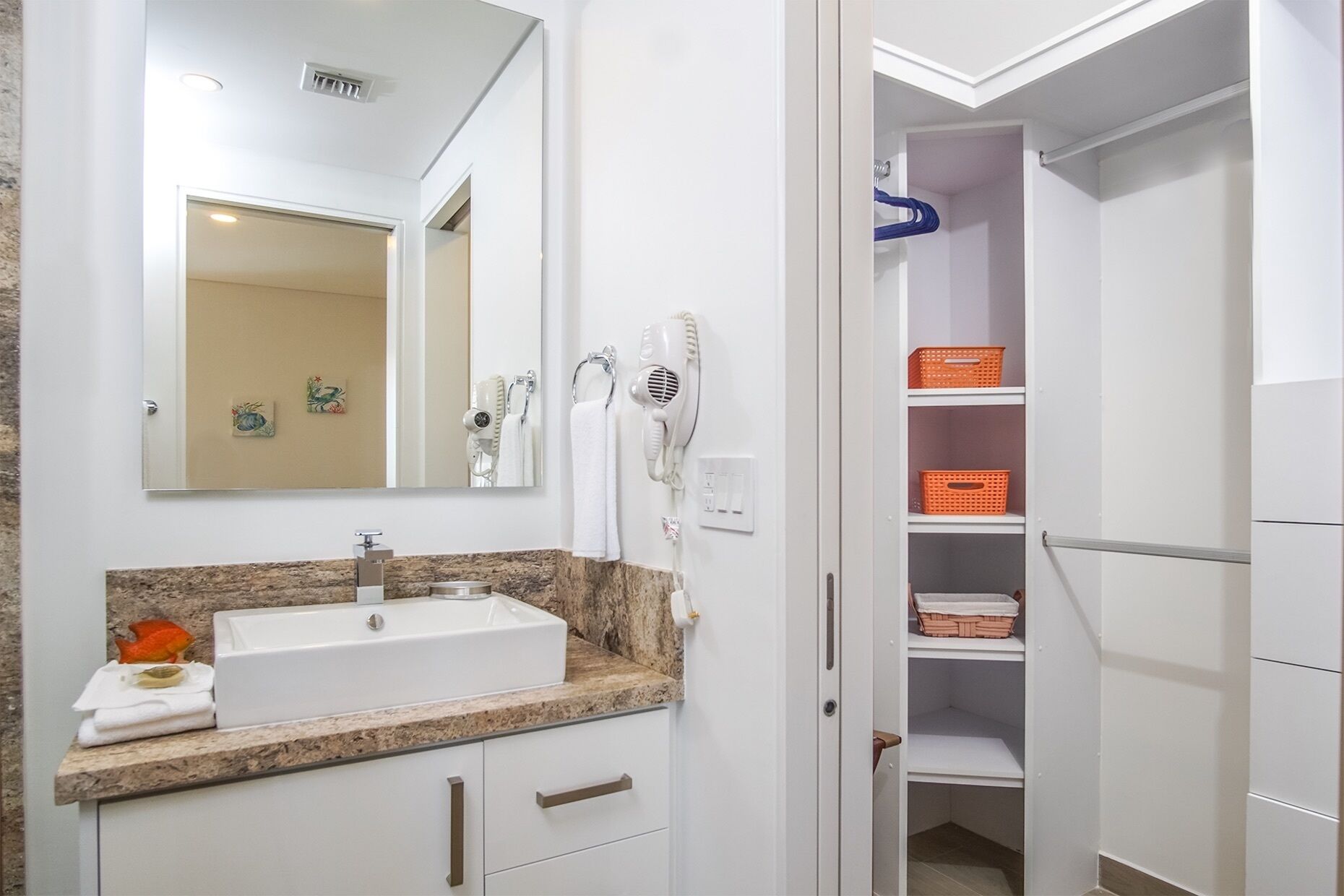 A bathroom with a sink, mirror, hair dryers, and storage shelves.