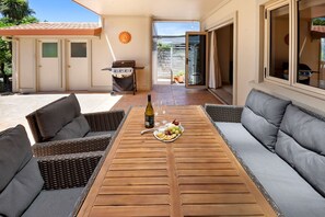 Un patio al aire libre con una mesa de madera, sillas de mimbre y una parrilla.