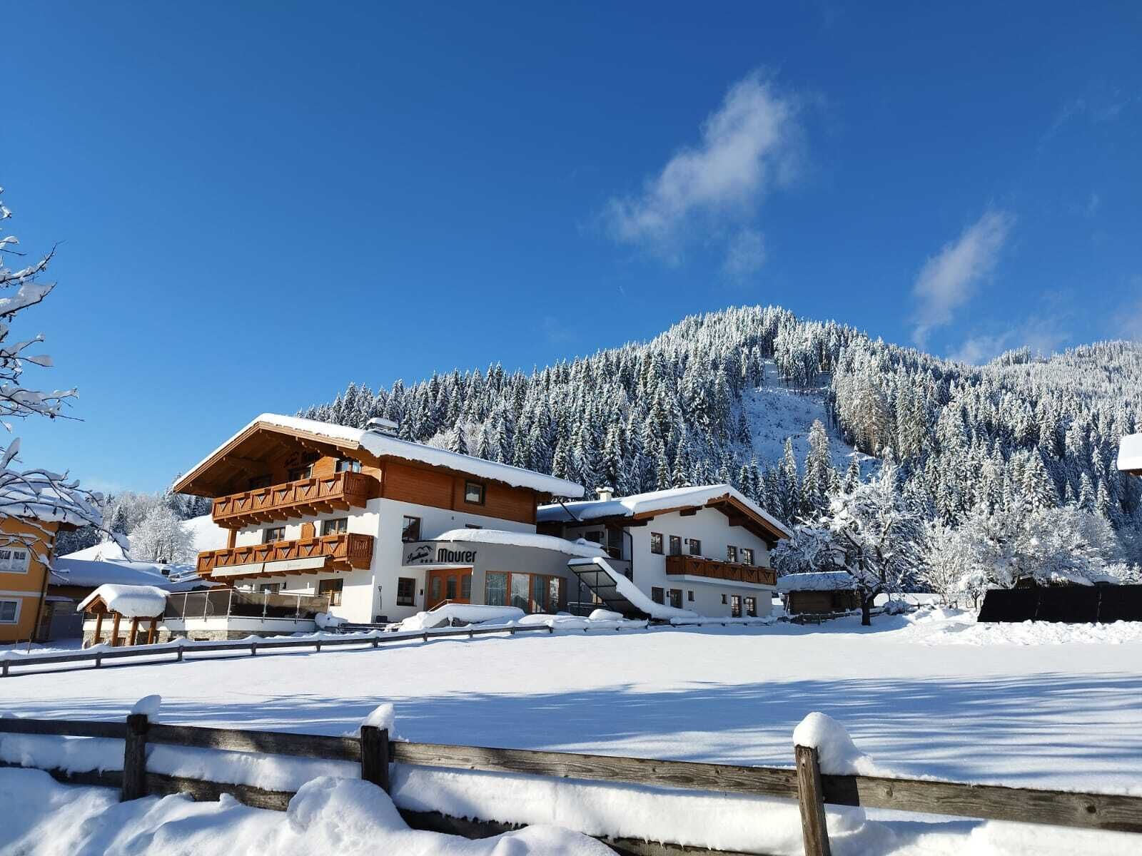 Een hotel in chaletstijl met een houten gevel, meerdere balkons en een besneeerd landschap met een berg op de achtergrond.