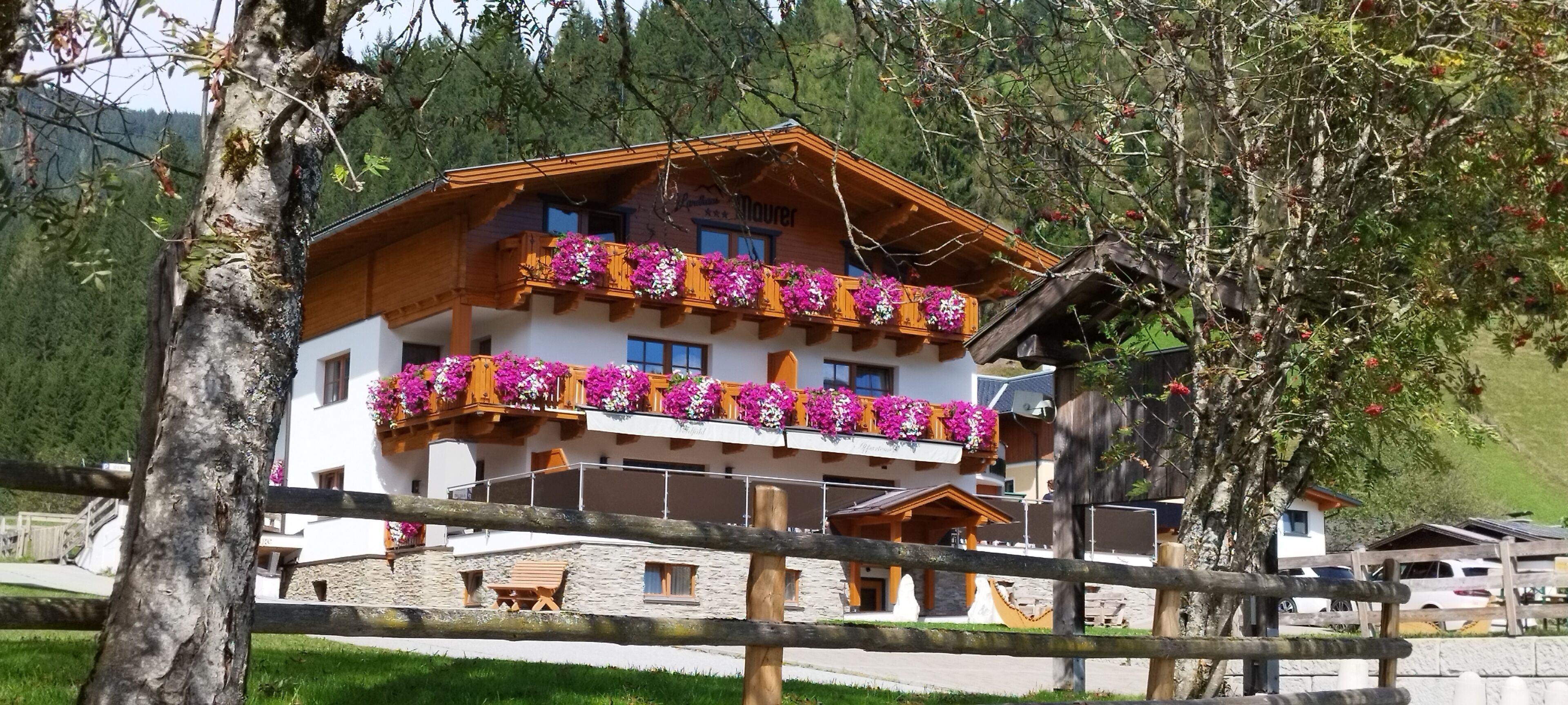 A two-story chalet with balconies adorned with flowers, set against a mountainous backdrop.