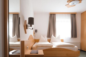 A hotel room with two beds, a bedside table, a lamp, and a window with curtains. - Landhaus Maurer (Wagrain)