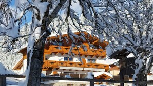 Um edifício de vários andares com estilo arquitetônico tradicional alpino, apresentando varandas de madeira e um ambiente coberto de neve.