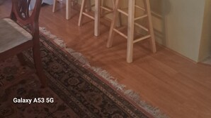 Een keuken met een marmeren aanrecht, houten krukken, een eethoek met een stoel en een klok aan de muur.