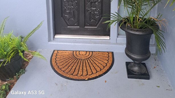 Een deur met daarboven het nummer '5363', een decoratieve krans, een potplant en een deurmat.