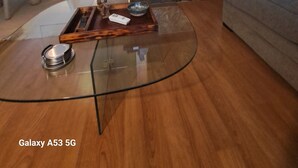 Een woonkamer met een glazen salontafel, een open haard, een bank en een eethoek op de achtergrond.