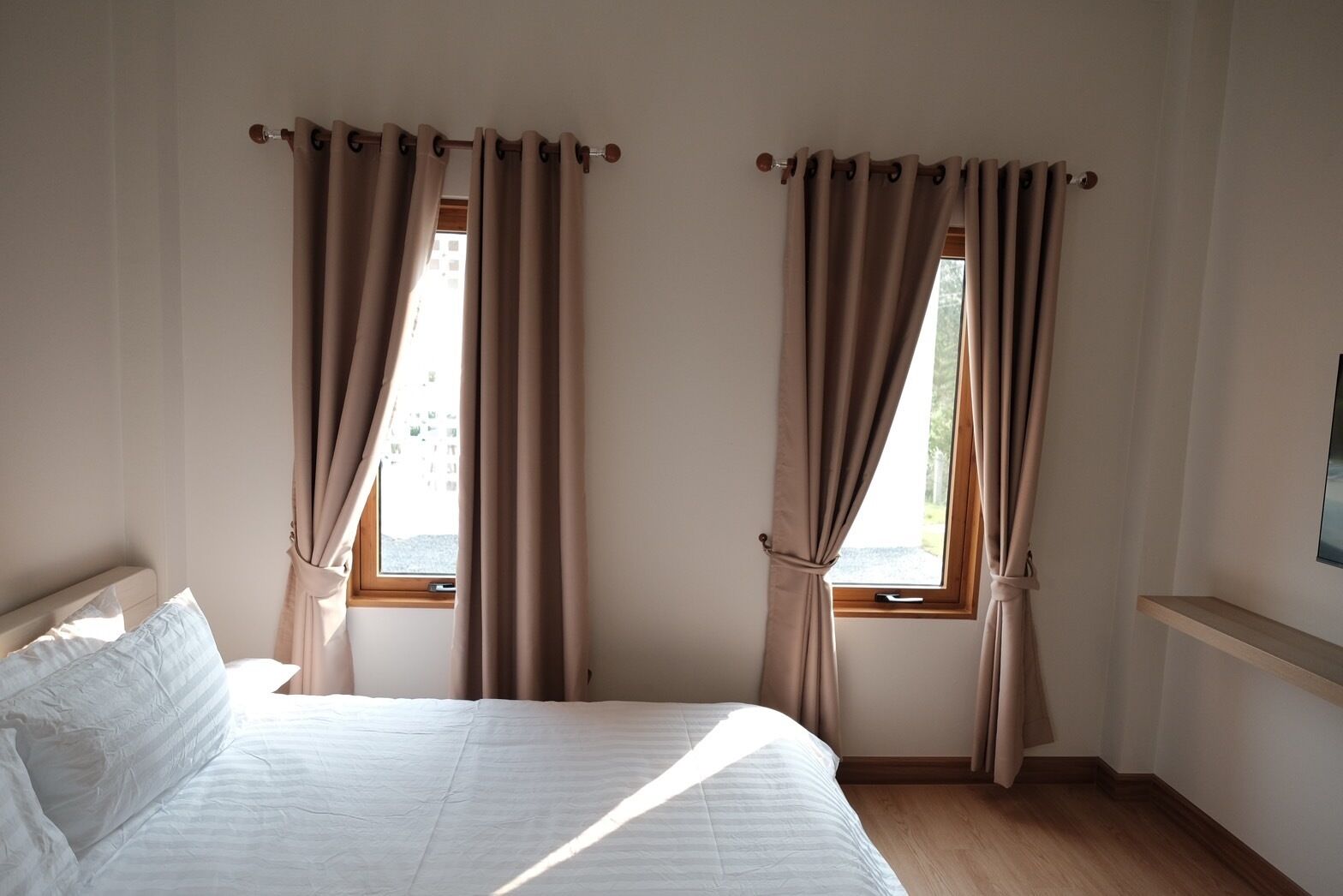 Quarto com cama, duas janelas com cortinas e piso de madeira.
