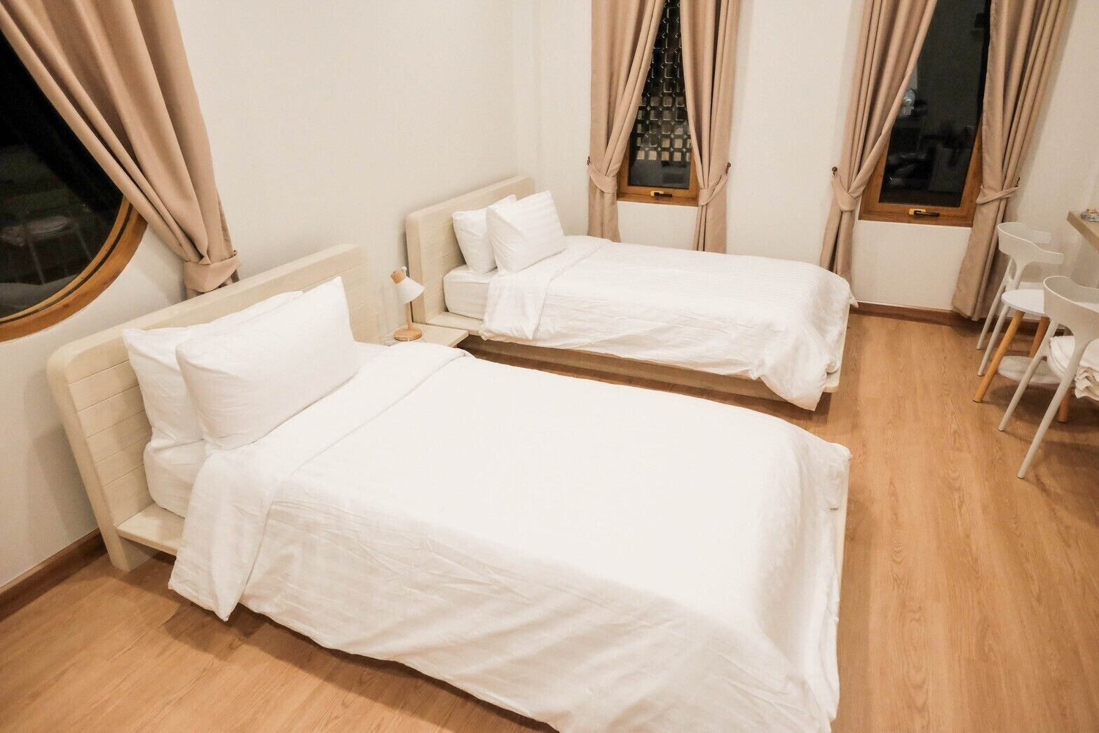 A hotel room with two single beds, a small table, and a chair.