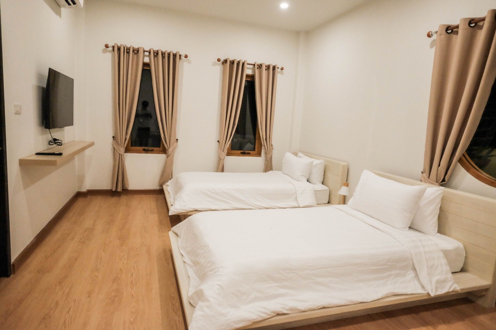 A hotel room with two beds, a TV on a shelf, and curtains on the windows.