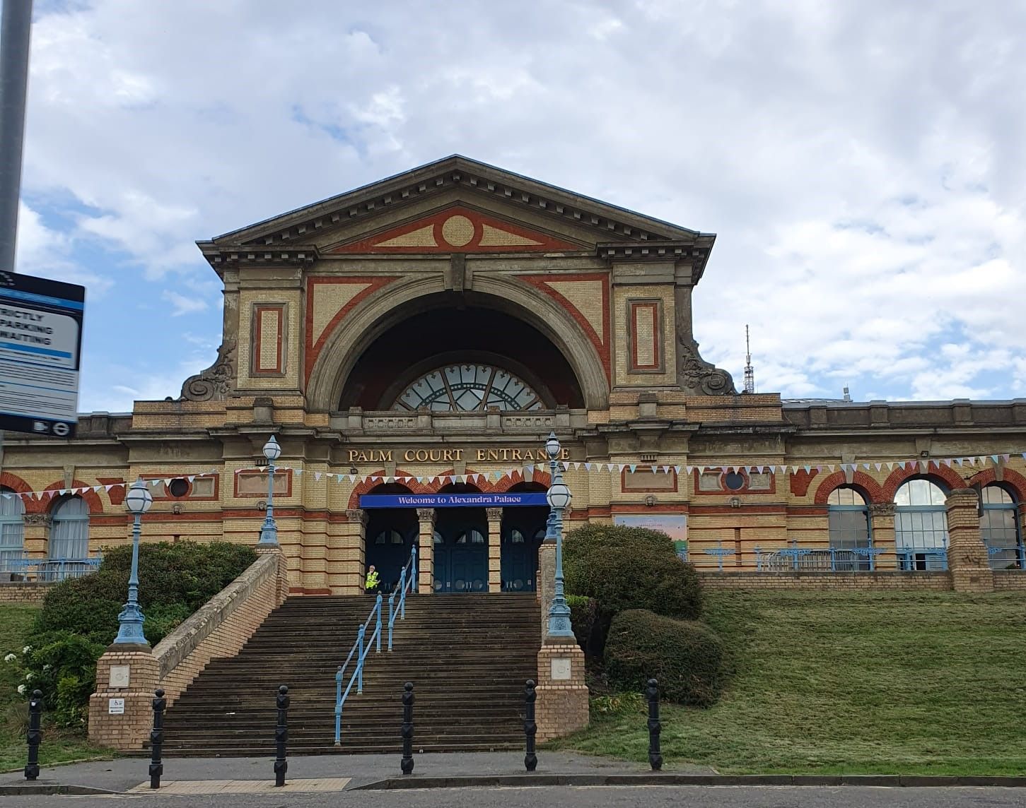 A grand entrance with a large archway, steps leading up to it, and a sign welcoming visitors to Alexandra Palace.