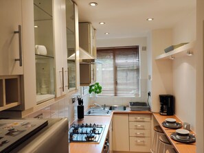 A modern kitchen with a gas stove, a sink, and a window with blinds.