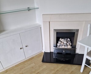 Una habitación con un armario blanco, una repisa de vidrio y una chimenea con leña.