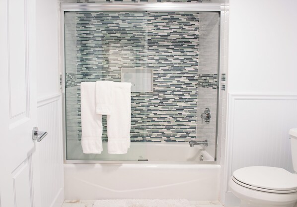 A bathroom with a glass-enclosed shower, a white toilet, and a white bathtub.
