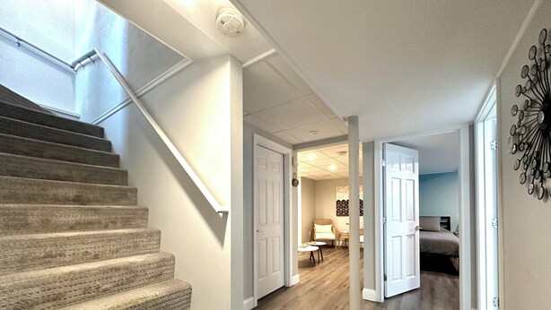 A staircase leading to a room with a wooden floor, a ceiling light, and a decorative wall piece. - Beachy Getaway Near Newport & Beaches (Middletown)