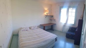 A bedroom with a bed, a desk, a chair, and a window.