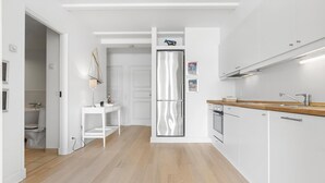 A modern kitchen with white cabinetry, a stainless steel refrigerator, and a wooden countertop.