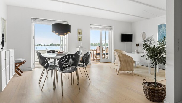 A spacious living area with a dining table, chairs, a TV, and a view of the water.