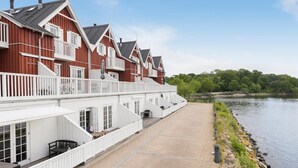 A row of red and white buildings with balconies overlooking a calm body of water.