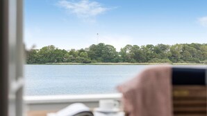 A room with a view of a lake, a wooden table with a book and a cup, and a window overlooking the water.