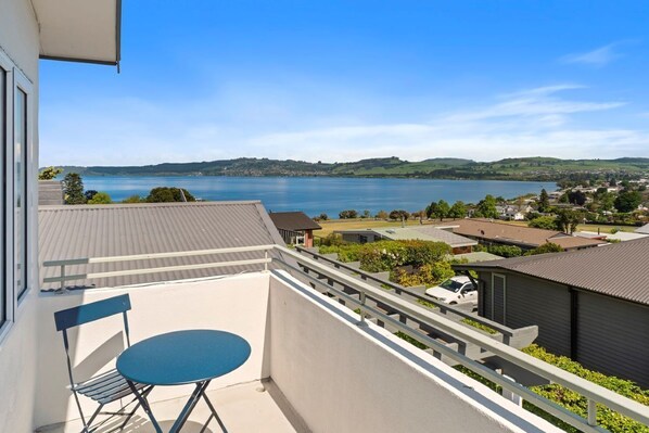A balcony with a blue table and chair, overlooking a lake and a town.