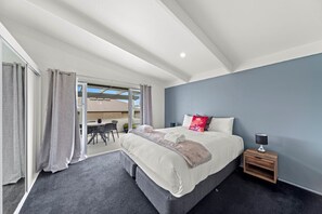 A bedroom with a large bed, a nightstand, a chair, and a view of the outside.