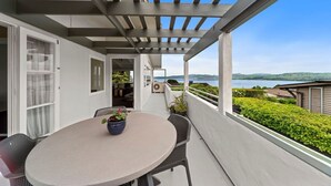 A balcony with a round table and chairs, a pergola overhead, and a view of a lake and hills. - Hilltop House Lake Views (Taupo)