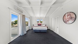 A bedroom with a large bed, a window with curtains, a wall-mounted air conditioning unit, and a framed picture. - Hilltop House Lake Views (Taupo)