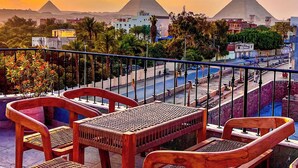A rooftop terrace with wooden furniture and a view of pyramids in the background. - Almas Pyramids View (Giza)