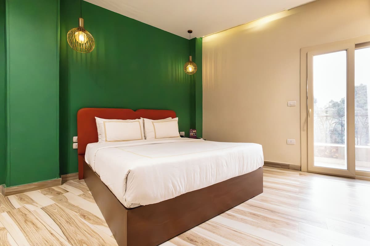 A bedroom with a large bed, green walls, and a sliding glass door to the outside.