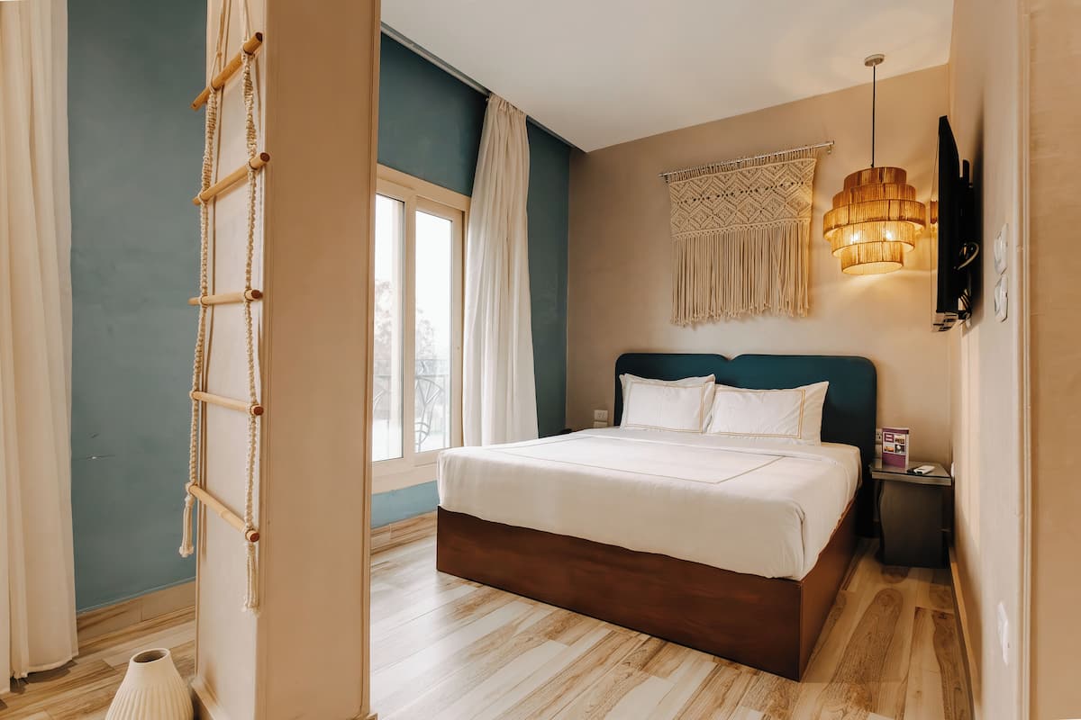 A bedroom with a bed, a bedside table, a wall-mounted TV, and a window with curtains.