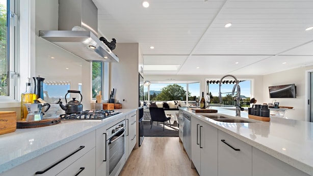 Een moderne keuken met een centraal eiland, ingebouwde apparatuur en grote ramen met uitzicht op de omgeving.