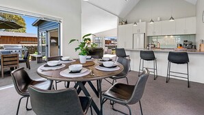 Et moderne køkken med hvide skabe, et spiseområde med et rundt bord og stole, samt et udendørs grillområde.