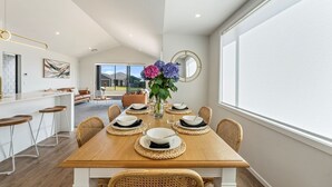 Un coin repas moderne avec une table en bois dressée pour six personnes, entourée de chaises en osier. Un vase rempli de fleurs est placé au centre.