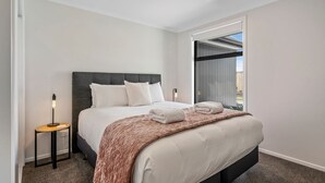 Une chambre d’hôtel moderne avec un grand lit, une table de chevet avec une lampe et une vue sur l’extérieur grâce à une porte coulissante.